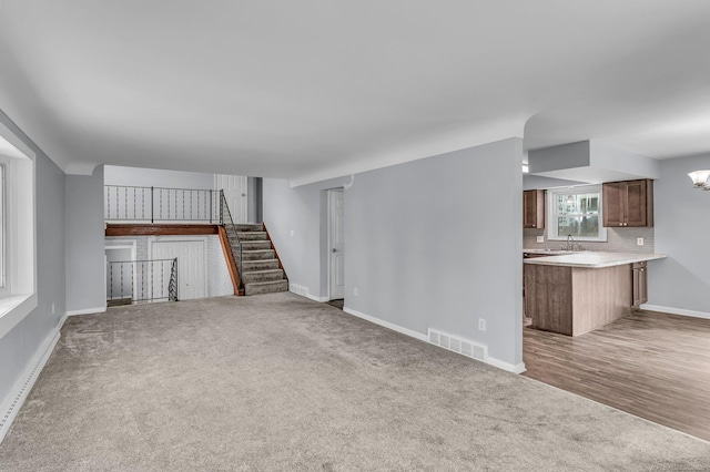 unfurnished living room featuring baseboards, visible vents, stairs, carpet flooring, and a sink