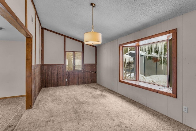 spare room with carpet, wooden walls, visible vents, and a textured ceiling