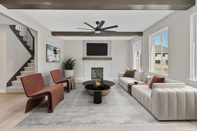 living room with visible vents, a tiled fireplace, stairway, wood finished floors, and beam ceiling