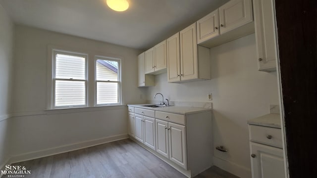 kitchen featuring white cabinets, light countertops, a sink, and light wood-style flooring