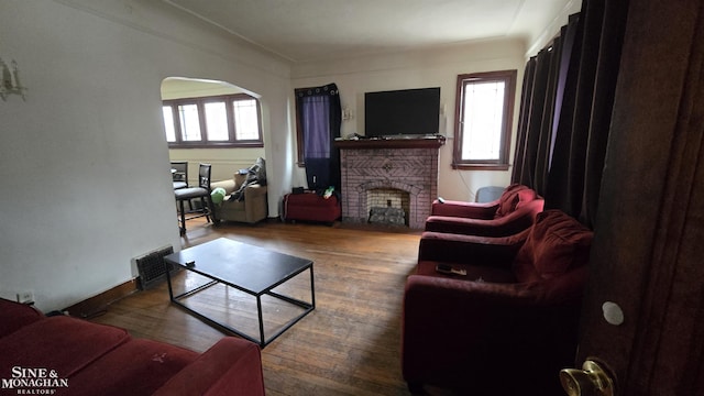 living area with a brick fireplace, visible vents, plenty of natural light, and wood finished floors