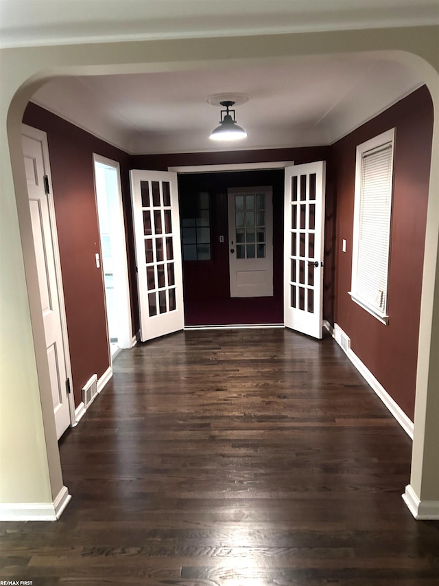 foyer entrance with arched walkways, visible vents, baseboards, and dark wood-style floors