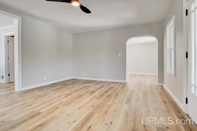 spare room featuring arched walkways, ceiling fan, a textured ceiling, light wood-type flooring, and baseboards