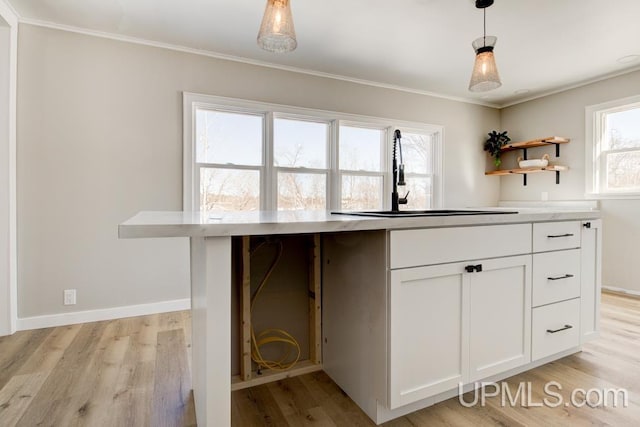 kitchen with white cabinets, ornamental molding, hanging light fixtures, light wood-type flooring, and a sink