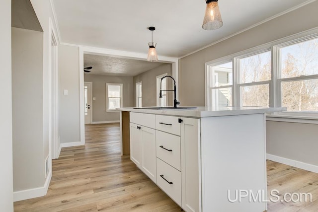 kitchen featuring light wood finished floors, hanging light fixtures, a kitchen island with sink, white cabinetry, and a sink