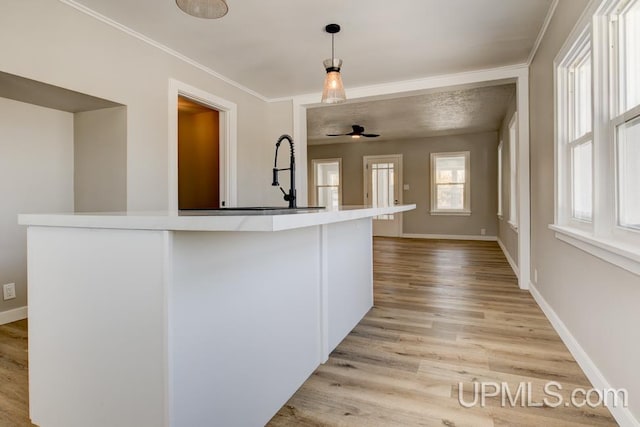 kitchen featuring baseboards, light wood-style floors, hanging light fixtures, light countertops, and crown molding