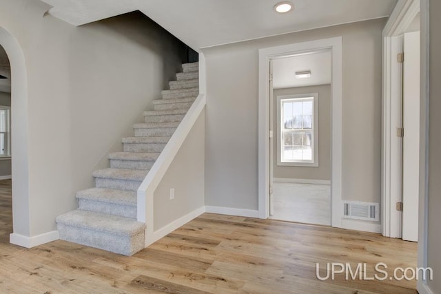 foyer entrance featuring baseboards, visible vents, arched walkways, wood finished floors, and stairs