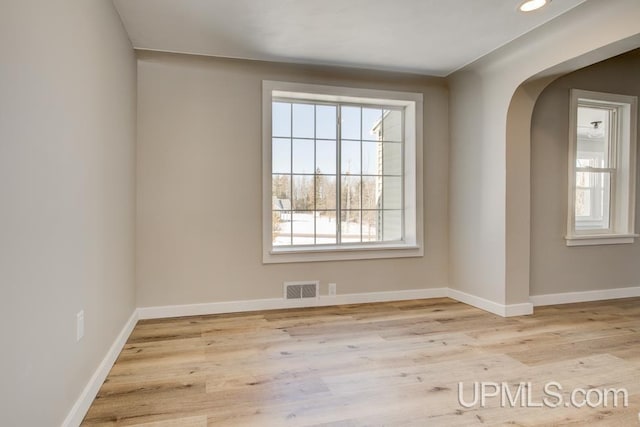 empty room with baseboards, visible vents, arched walkways, and wood finished floors