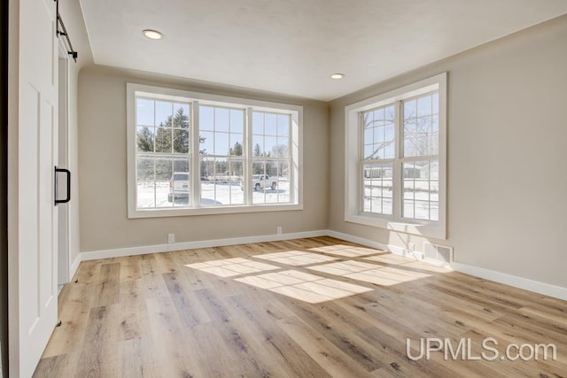 spare room featuring a barn door, recessed lighting, wood finished floors, and baseboards