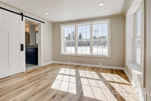 spare room with a barn door, baseboards, light wood-style flooring, and recessed lighting