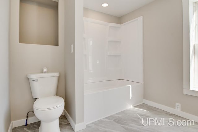 bathroom with toilet, washtub / shower combination, and baseboards