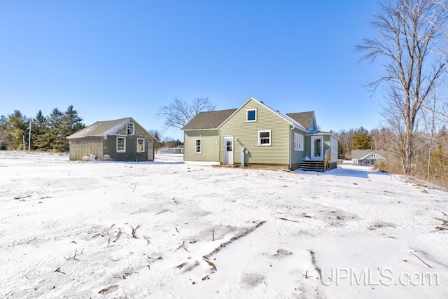 snow covered back of property featuring an outdoor structure