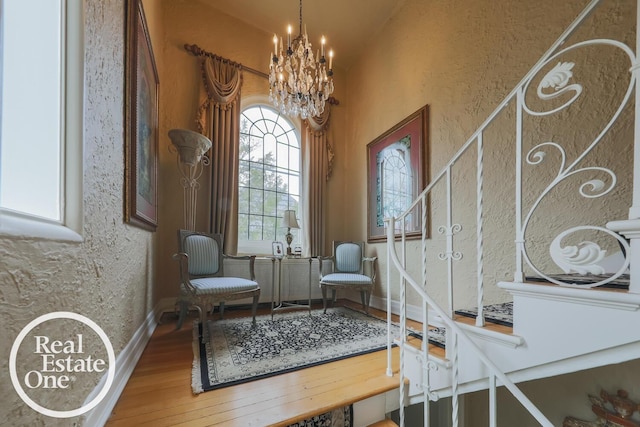 living area with an inviting chandelier, baseboards, wood finished floors, and a textured wall