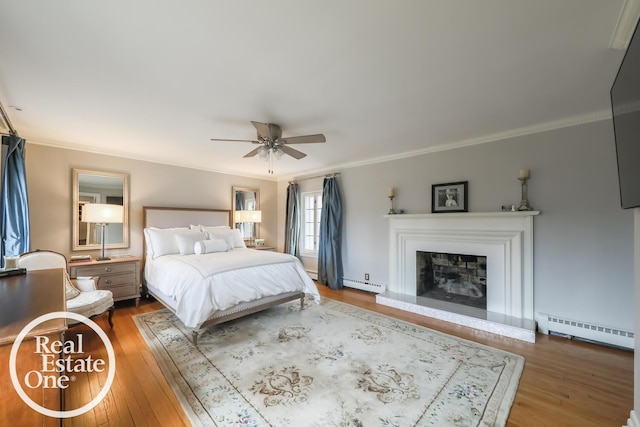 bedroom with a fireplace with raised hearth, a baseboard radiator, wood finished floors, ornamental molding, and baseboard heating