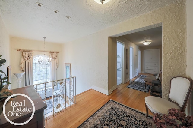 hall with a textured wall, a textured ceiling, an upstairs landing, wood finished floors, and a chandelier