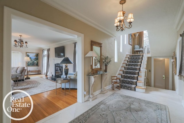 tiled entrance foyer with stairs, ornamental molding, a glass covered fireplace, and an inviting chandelier