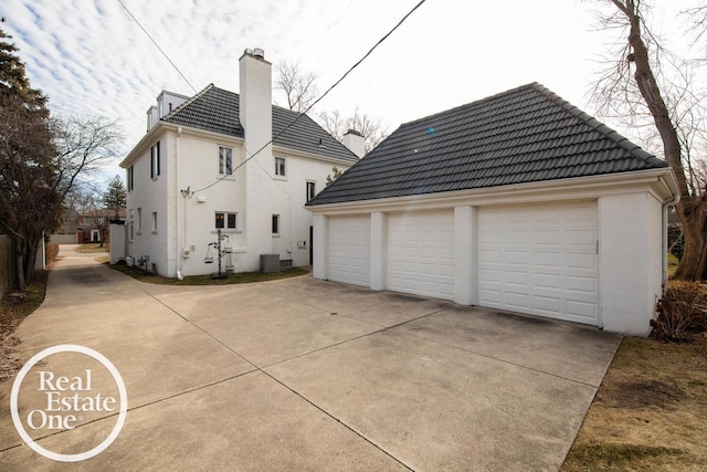 exterior space featuring a garage, a tiled roof, an outdoor structure, and stucco siding