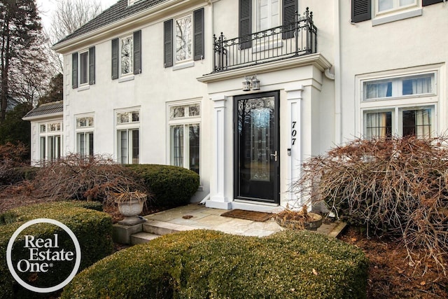 view of exterior entry featuring a balcony and stucco siding