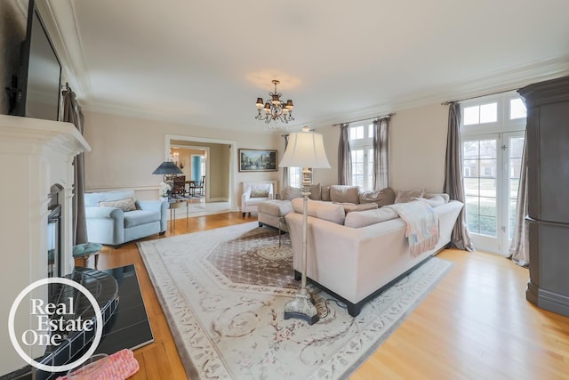 living area with ornamental molding, a chandelier, a fireplace, and light wood-style floors