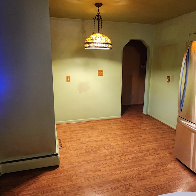 empty room featuring light wood-type flooring, arched walkways, visible vents, and baseboards