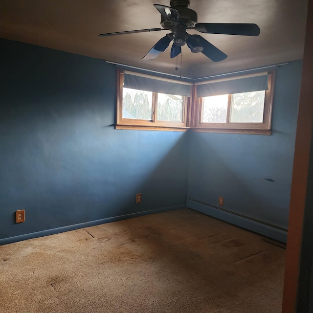 carpeted spare room featuring a ceiling fan, baseboard heating, a wealth of natural light, and baseboards