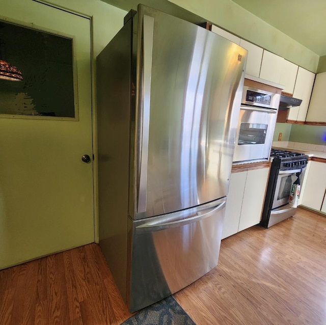 kitchen featuring light wood-style flooring, under cabinet range hood, stainless steel appliances, white cabinetry, and light countertops