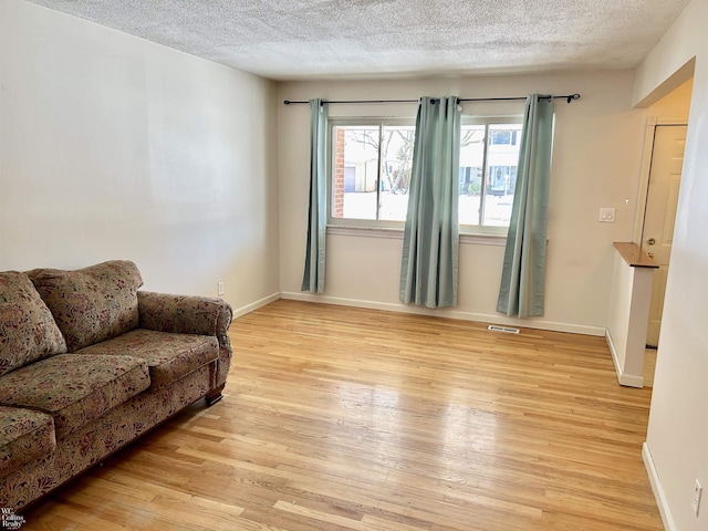 living room featuring a textured ceiling, light wood finished floors, and baseboards