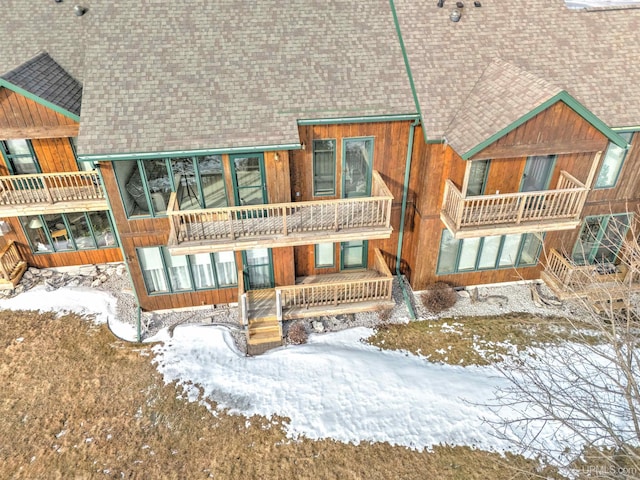 snow covered property with roof with shingles