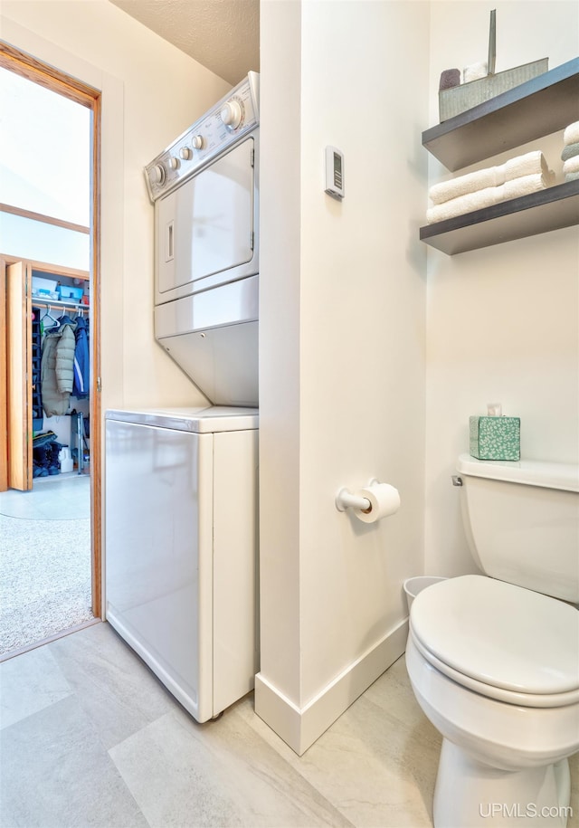 bathroom with baseboards, toilet, and stacked washer / drying machine