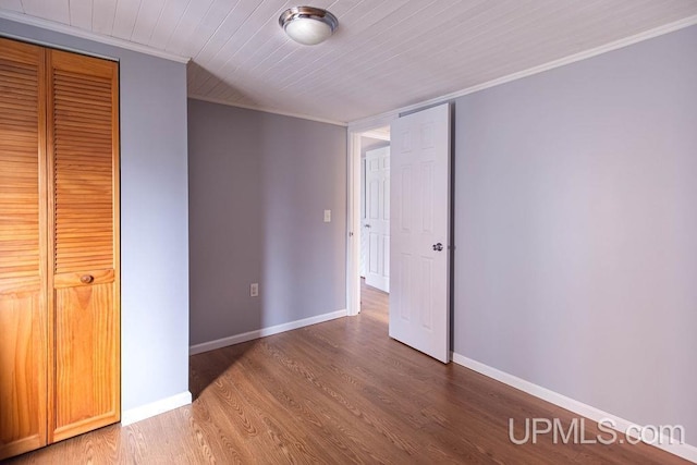 unfurnished bedroom featuring a closet, ornamental molding, wood finished floors, wooden ceiling, and baseboards