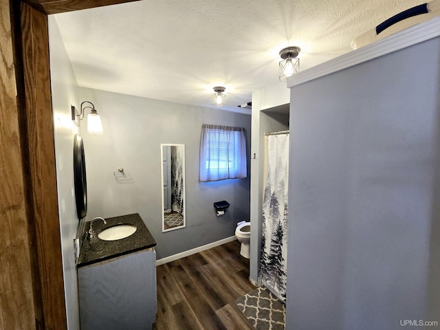 bathroom featuring toilet, a textured ceiling, wood finished floors, baseboards, and vanity