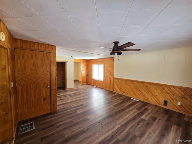 empty room featuring dark wood-type flooring, visible vents, wood walls, and ceiling fan