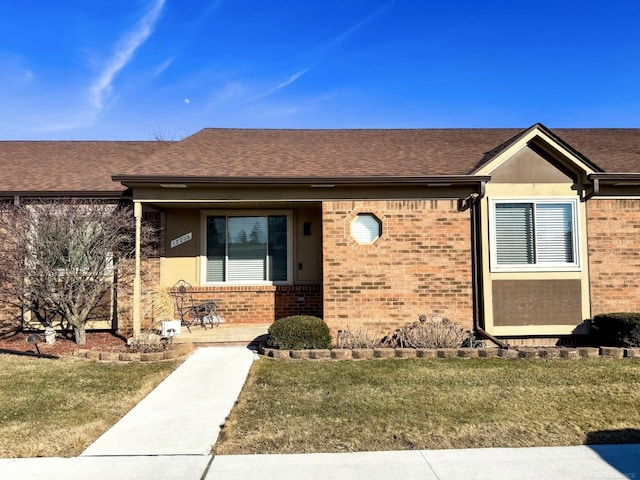 view of front of house featuring a front yard, covered porch, brick siding, and roof with shingles