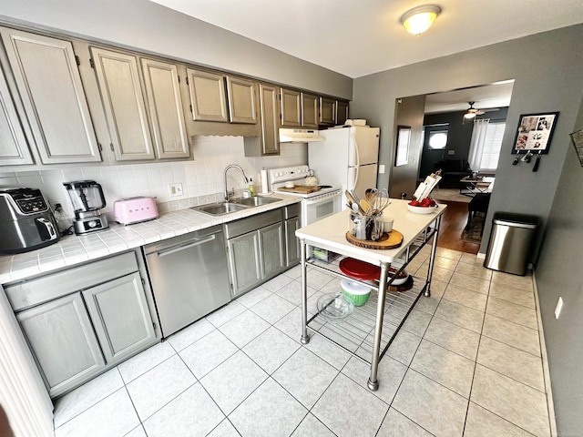 kitchen featuring a sink, under cabinet range hood, white appliances, light tile patterned floors, and tile counters