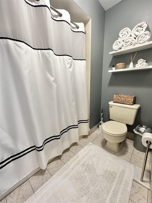 bathroom featuring curtained shower, toilet, baseboards, and marble finish floor