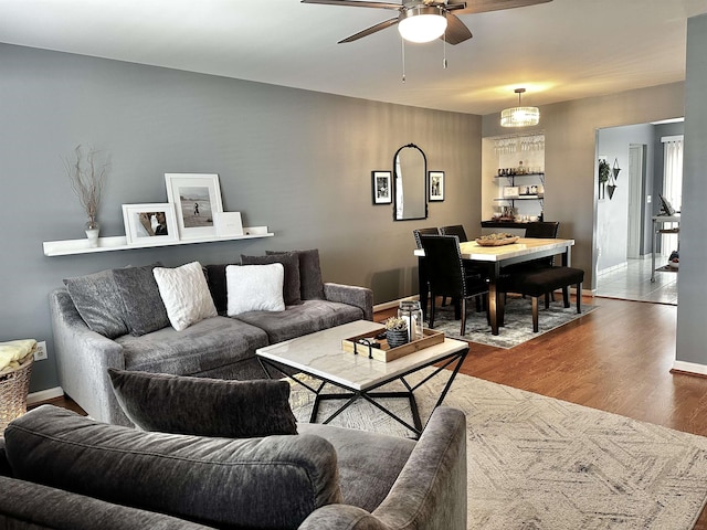 living room featuring baseboards, a ceiling fan, and dark wood-style flooring