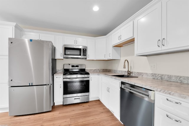 kitchen with light wood-style flooring, a sink, stainless steel appliances, light countertops, and white cabinets