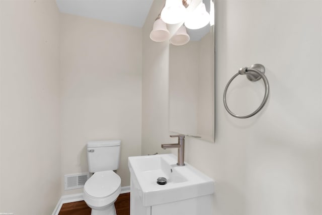 half bathroom featuring visible vents, toilet, wood finished floors, baseboards, and vanity