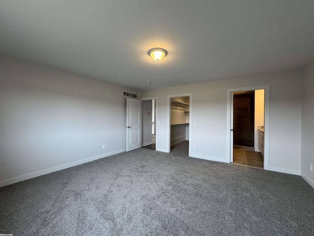 unfurnished bedroom featuring visible vents, baseboards, a spacious closet, and dark carpet