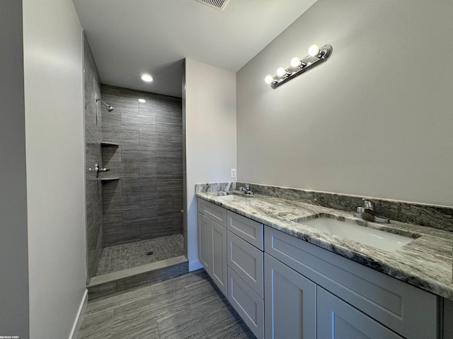 bathroom featuring a tile shower, double vanity, baseboards, and a sink