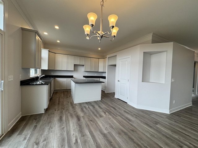 kitchen with wood finished floors, a kitchen island, ornamental molding, dark countertops, and a notable chandelier