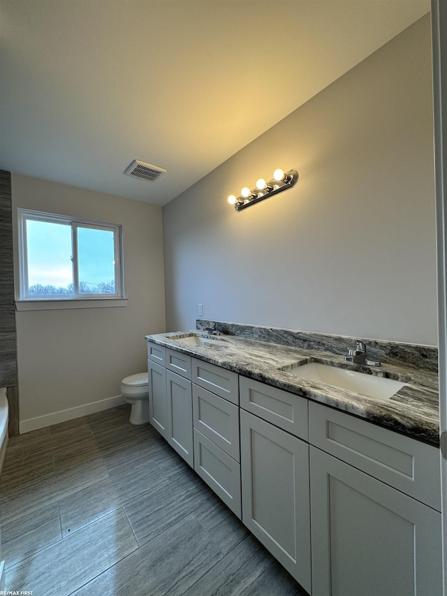 bathroom featuring double vanity, visible vents, toilet, and a sink