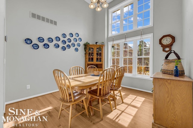 dining room featuring visible vents, baseboards, a high ceiling, and light wood-style floors