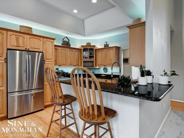 kitchen with baseboards, a breakfast bar, light wood-style flooring, freestanding refrigerator, and glass insert cabinets