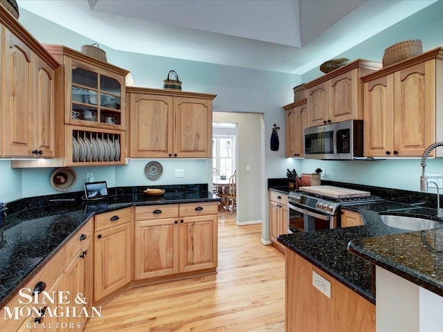 kitchen featuring a sink, stainless steel microwave, gas range oven, light wood finished floors, and glass insert cabinets