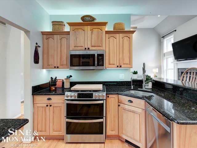 kitchen with a sink, dark stone countertops, light brown cabinets, and stainless steel appliances