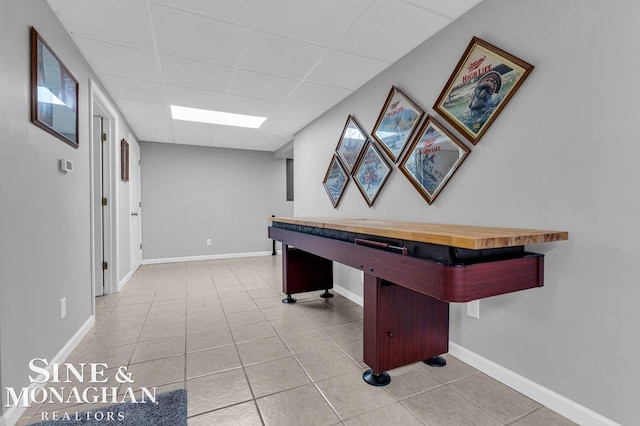 recreation room with tile patterned flooring, a drop ceiling, and baseboards