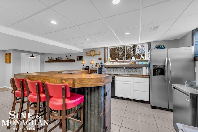 kitchen featuring butcher block counters, a breakfast bar area, stainless steel refrigerator with ice dispenser, light tile patterned flooring, and white cabinets