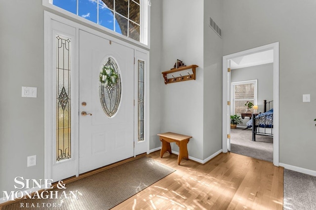 foyer featuring visible vents, baseboards, light wood-style floors, and a towering ceiling