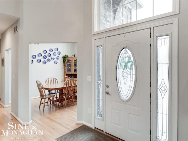 entrance foyer with visible vents, light wood-style flooring, baseboards, and a towering ceiling